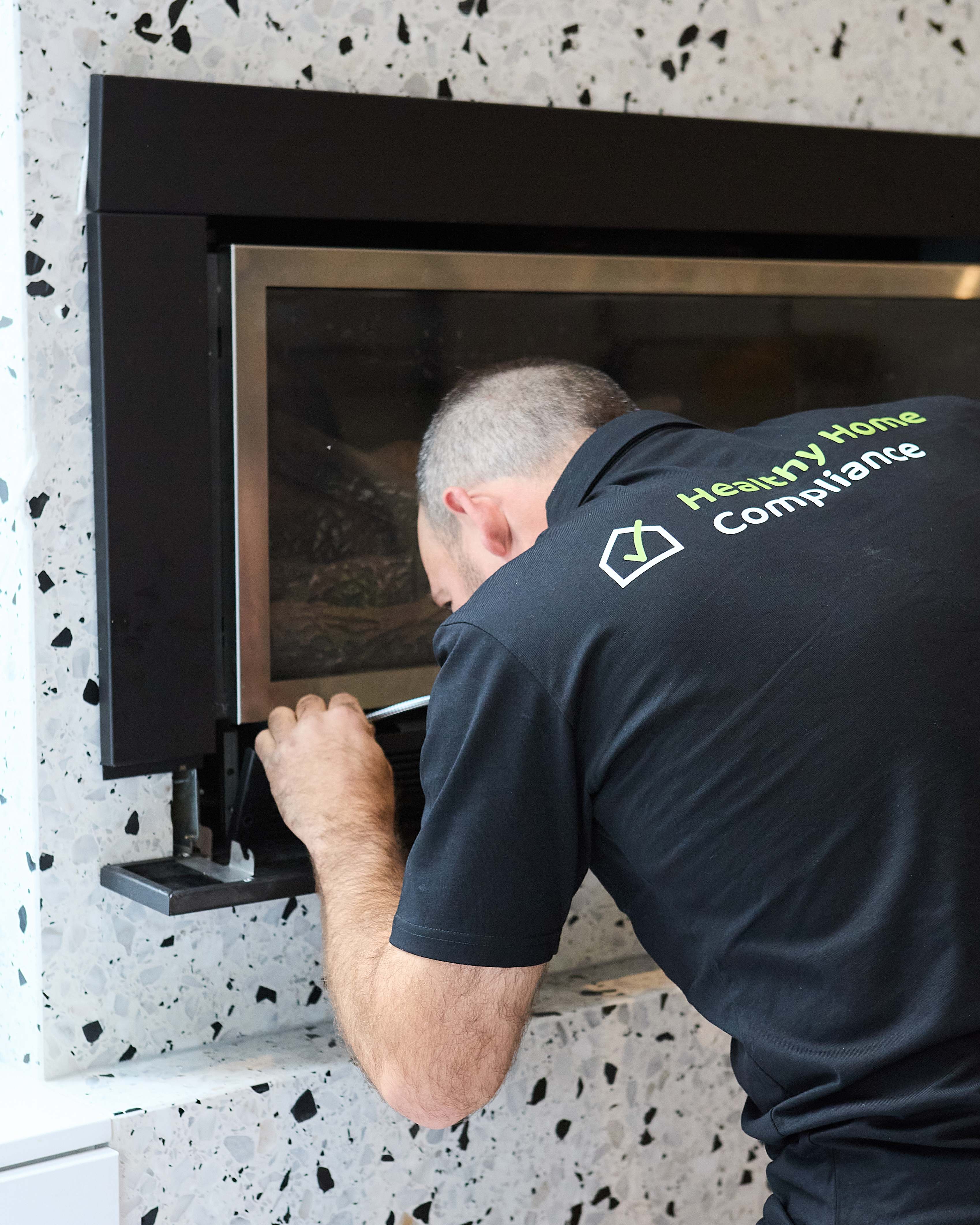 Healthy Home Compliance technician inspecting a gas fireplace — branded polo with logo